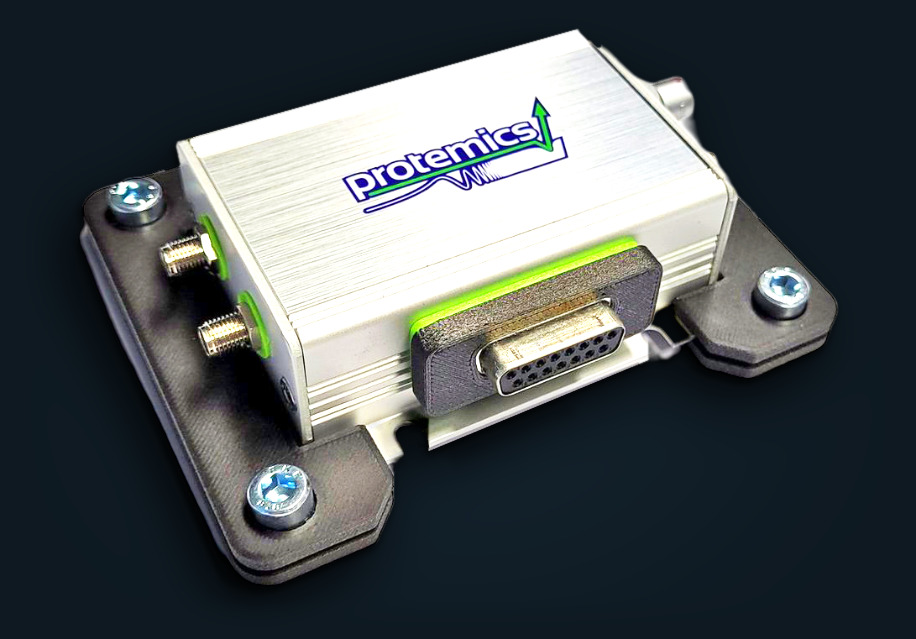 Photograph of the TS Companion amplifier: brushed aluminium housing with Protemics logo on a black mounting plate, two SMA input connectors and a 15-pin Sub-D control connector.