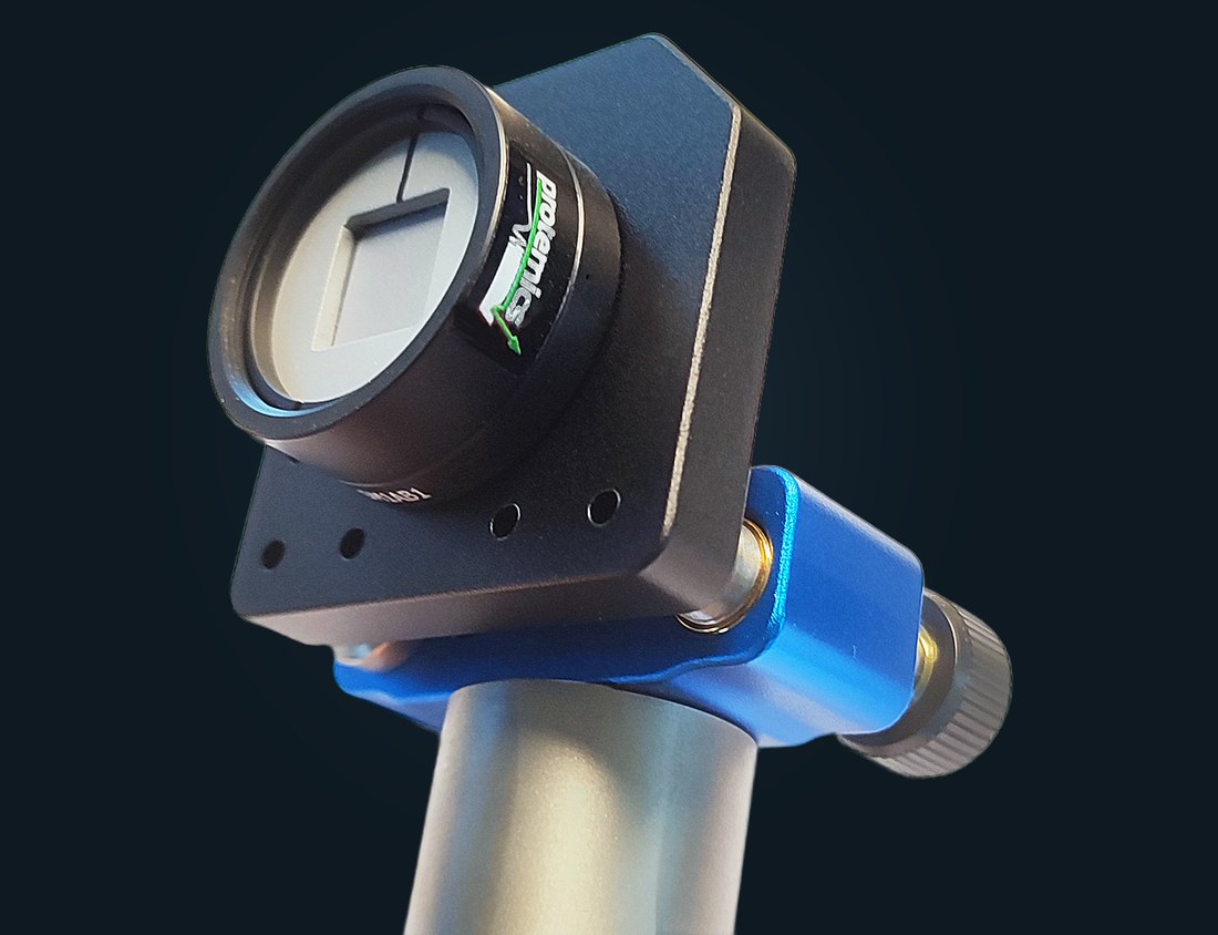 Photograph of the TeraBlast emitter in its black 1-inch housing with Protemics label, held in a mounting plate on an optical post with a blue post holder; the emitter chip is visible behind the front window.