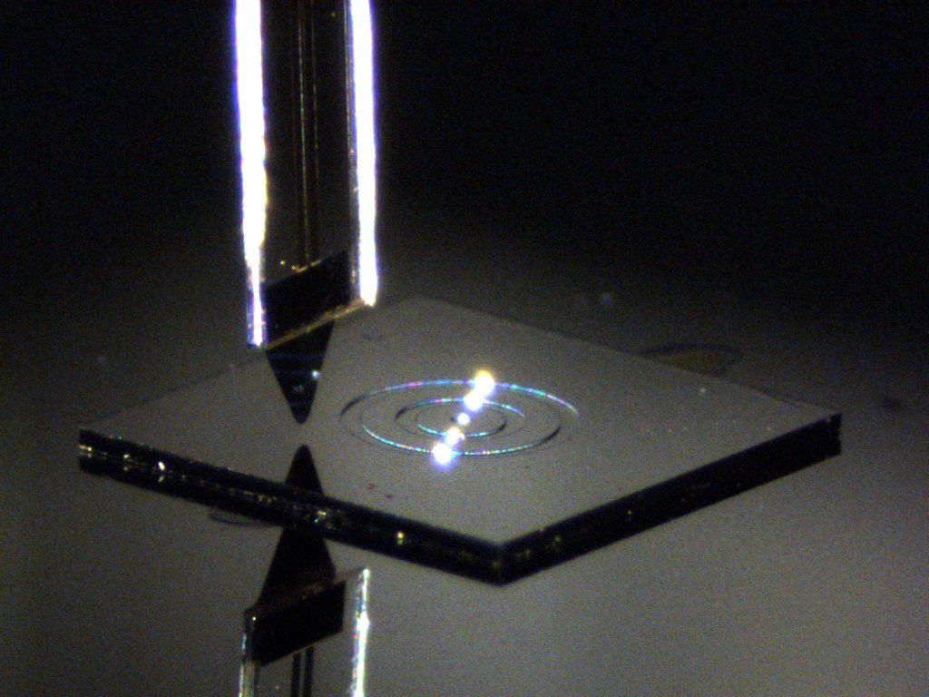 Photograph of a TeraSpike near-field probe tip held just above a glass calibration sample with a concentric ring structure; the THz emitter is visible below the sample.